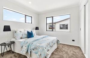 a white bedroom with a bed and two windows at Holiday Home at Huia Road in Auckland