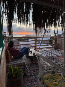 Tamraght OuzdarにあるNatural Surf Houseのベンチに腰掛けて夕日を眺める女