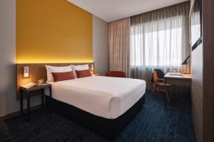 シドニーにあるリッジズ シドニー エアポート ホテルの大きなベッドとデスクが備わるホテルルームです。