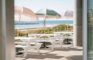 a group of white tables and umbrellas on a balcony at Glenelg Oasis, Pool, Gym, Spa & Sauna, Free Parking, City Views in Glenelg