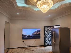 TV en la pared en una habitación con lámpara de araña en الجبيل, en Al Jubail