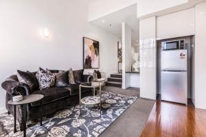 ein Wohnzimmer mit einem schwarzen Sofa und einem Kühlschrank in der Unterkunft VAQUAY Fifth Avenue In Melbourne CBD in Melbourne