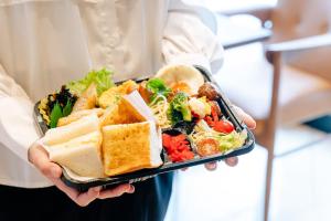 a woman is holding a tray of salad and sandwiches at Hotel Hillarys in Osaka