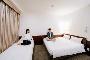 two people sitting on beds in a hotel room at Hotel Hillarys in Osaka