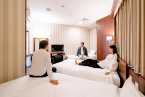 three people sitting on beds in a hotel room at Hotel Hillarys in Osaka