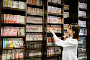 Una mujer parada en una biblioteca mirando DVD en Hotel Hillarys en Osaka