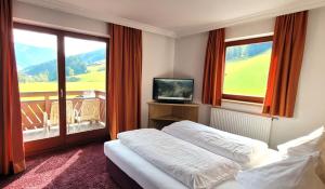a bedroom with a bed and a television and a balcony at Hotel Sommerer - inklusive JOKER CARD im Sommer in Saalbach Hinterglemm