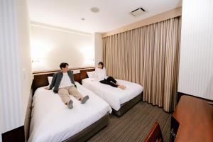 Dos personas sentadas en camas en una habitación de hotel en Hotel Hillarys en Osaka