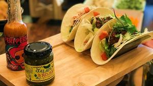 two tacos on a cutting board next to a bottle of sauce at Via Inn Shinjuku in Tokyo