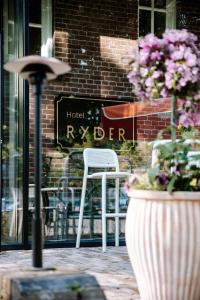 Hotel Ryder I Den Bosch - Vught في سيرتوخيمبوس: كرسي أبيض و مزهرية مع الزهور أمام المبنى