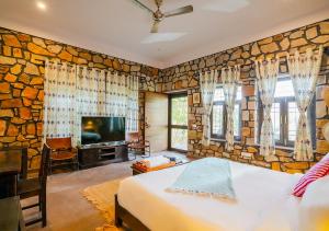 a bedroom with a stone wall with a bed and a tv at Moustache Ranthambore Luxuria in Sawāi Mādhopur
