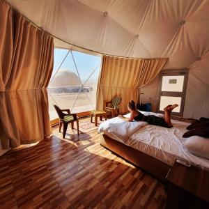 Wadi Rum Classic camp في العقبة: شخص يستلقي على سرير في خيمة