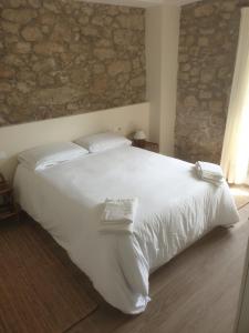 Una cama blanca en un dormitorio con una pared de piedra. en La Casa de Ana en Fisterra, en Finisterre