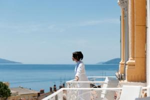 a woman standing on a balcony looking out at the ocean at BRISTOL Hotel Opatija in Opatija