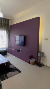 unique 2 rooms apartment al madina st amman في Umm Uthainah: غرفة معيشة مع جدار أرجواني مع تلفزيون بشاشة مسطحة