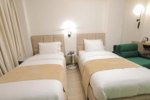 two beds in a hotel room with a green chair at Olia Residence in Tirana