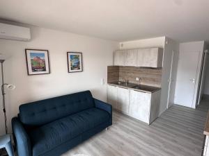 a living room with a blue couch and a kitchen at Appartement T2 avec piscine et vue mer proche plages - FR-1-768-76 in Les Issambres