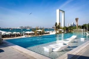 a swimming pool with white lounge chairs and the ocean at La Vie in Dubai