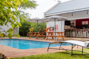 a swimming pool with two tables and an umbrella at PheZulu Guest Lodge in Victoria Falls