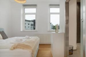 a white bedroom with a bed and two windows at Zeitlos Zuhause Bregenz in Bregenz
