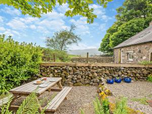 a wooden picnic table in a garden with a stone wall at 1 Bed in Eskdale 94530 in Eskdale