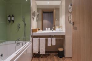 een badkamer met een wastafel, een bad en een spiegel bij Pena Park Hotel in Ribeira de Pena