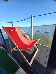 a red chair sitting on the deck of a boat at ARKA 1 domki na wodzie w Mielnie, rower wodny, bezpłatny WIFI, Parking in Mielno