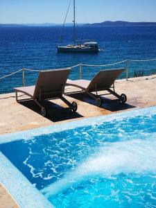 duas cadeiras sentadas ao lado de uma piscina com um barco em Bella Vista apartments with hot pool and jacuzzi em Trogir