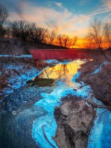 a red bench sitting next to a river with snow at Iowa Nice, Winterset in Winterset