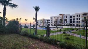 um parque com palmeiras e um edifício em Plage dès nations 2 bedroom apartment with backyard view em Sidi Bouqnadel