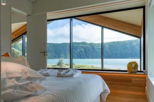 a bedroom with a large window looking out at the water at Sete Cidades Lake Cabin - Casa da Lagoa in Ponta Delgada