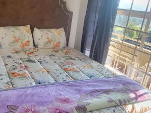 a bed with a purple comforter and a window at ENTIRE LUXURY APARTMENTS in Mbabane