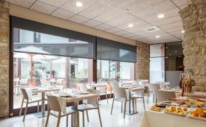 un restaurante con mesas y sillas blancas y ventanas en Casa Marcial (adults only), en Besalú