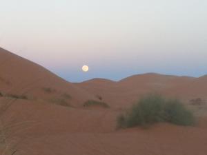 una puesta de sol en el desierto con la luna en el cielo en RiadSuerteloca Merzouga en Merzouga