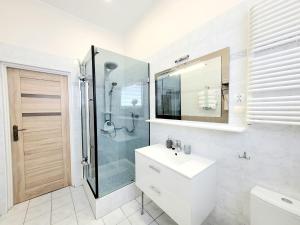 a white bathroom with a shower and a sink at Apartamenty Cudowna Wyspa in Świnoujście