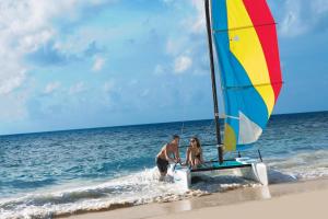 un hombre y una mujer en la playa con un velero en Dreams Sapphire Resort & Spa, en Puerto Morelos