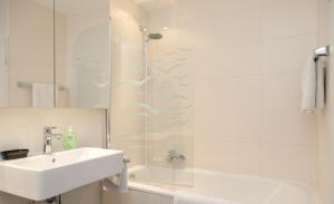 ein weißes Bad mit einem Waschbecken und einer Dusche in der Unterkunft Boarding House "Herzogpark Celle" in Celle
