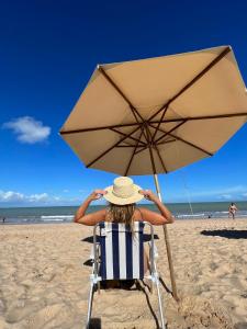 uma mulher sentada numa cadeira debaixo de um guarda-sol na praia em Kastel Jampa Hotel em João Pessoa