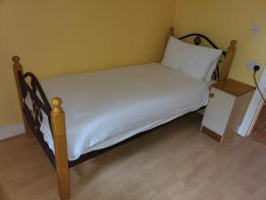 a bed with a wooden frame and white sheets and a night stand at Sheraton Lodge Apartments T12 E309 in Cork