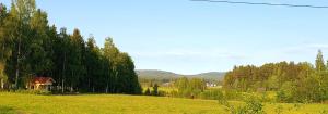 a field with a house in the middle of a field with trees at Skålbo gårdsglamping in Järvsö