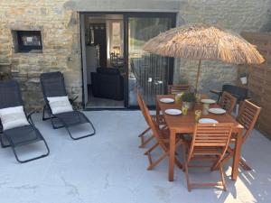 a wooden table with chairs and an umbrella on a patio at Le Cottage d'Emmy - Rose in Commes