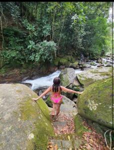 Uma mulher de biquíni cor-de-rosa a caminhar sobre rochas perto de um rio. em Pousada Estação Boca do Mato em Cachoeiras de Macacu