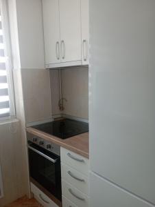 una pequeña cocina con armarios blancos y estufa negra en Apartman Dragon Kg en Kragujevac