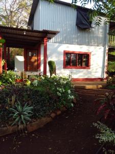 uma pequena casa branca com uma janela vermelha em Jungle Vacation Home with river and waterfall. em Santa Rita