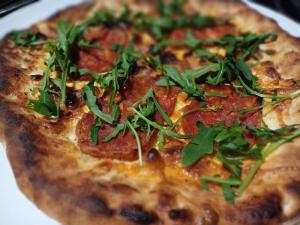 uma pizza com pepperoni e verduras num prato em NORA Guesthouse and Restaurant em Zamárdi