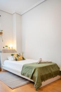 een witte slaapkamer met een bed met een groene deken bij Luxotica Gardens Valencia in Valencia