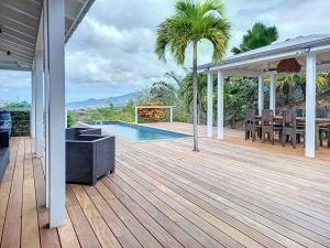 eine Holzterrasse mit einem Pool auf einem Haus in der Unterkunft Villa vue mer et montagne Pelée in Le Carbet