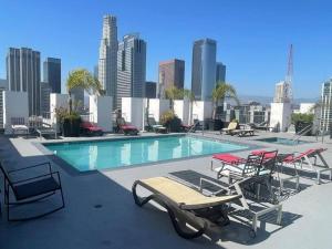 a swimming pool with lounge chairs and a city skyline at Sky-Rise Apartments in Los Angeles