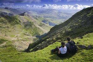 ドルゲラウにあるY Meirionnydd Townhouseの二人の人が谷を見ながら丘の上に座っている