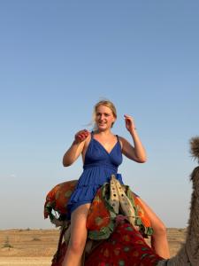 Una mujer con un vestido azul está sentada en un camello en Best Desert Camp In Jaisalmer Red Velvet, en Jaisalmer